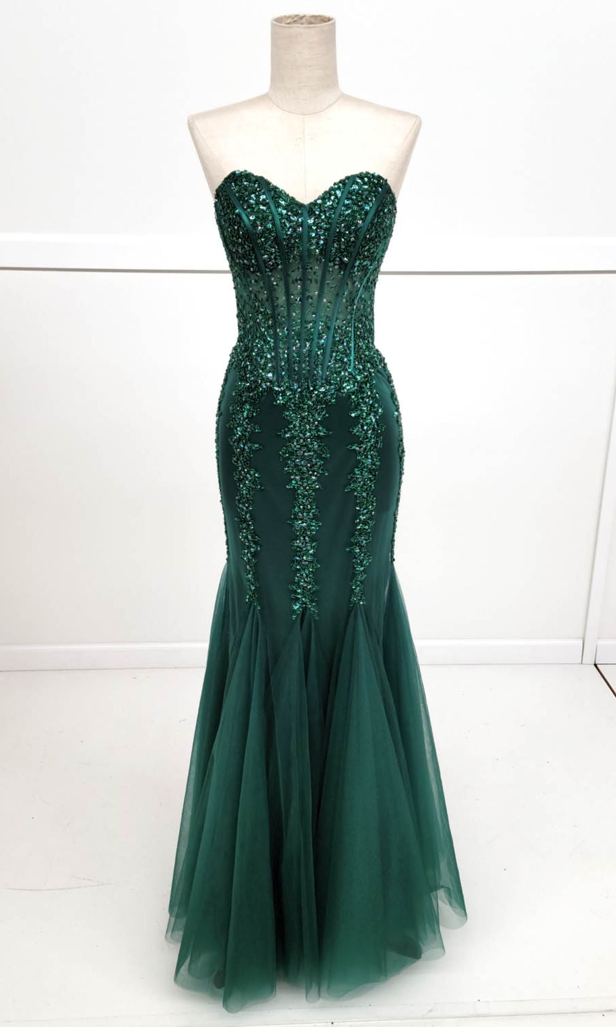 The Strapless Long Mermaid Prom Dress: Chicas C820 is a dark green gown with a fitted beaded bodice and flowing tulle mermaid skirt, shown on a dress form against a simple background.